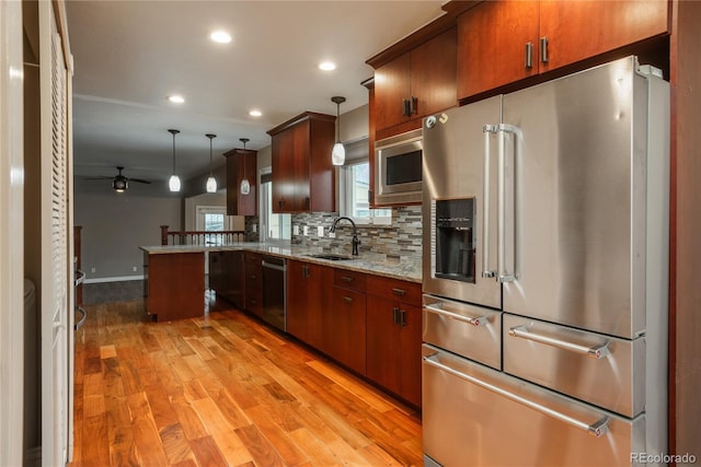 kitchen with backsplash, appliances with stainless steel finishes, a peninsula, light wood-style floors, and a sink