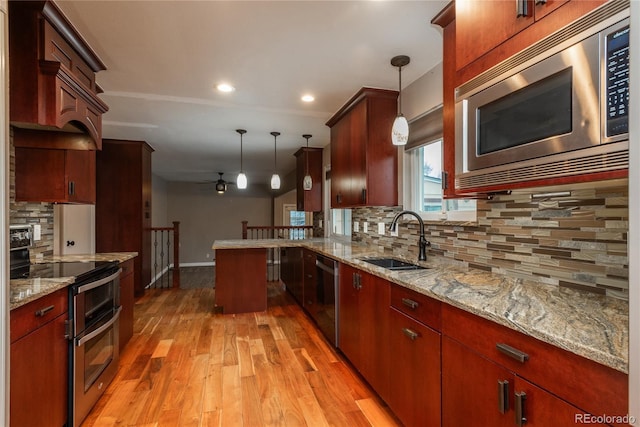 kitchen with light wood finished floors, a peninsula, a sink, hanging light fixtures, and appliances with stainless steel finishes