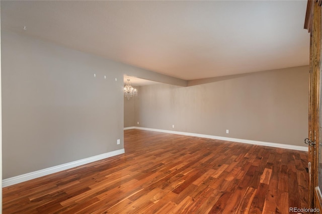 unfurnished room featuring a notable chandelier, baseboards, and wood finished floors