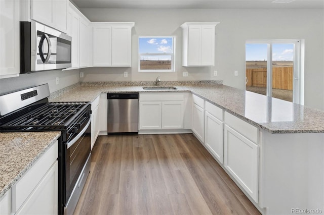 kitchen with appliances with stainless steel finishes, white cabinetry, a sink, wood finished floors, and a peninsula