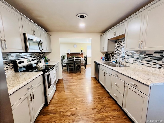 kitchen featuring light stone counters, stainless steel appliances, white cabinets, a sink, and wood finished floors