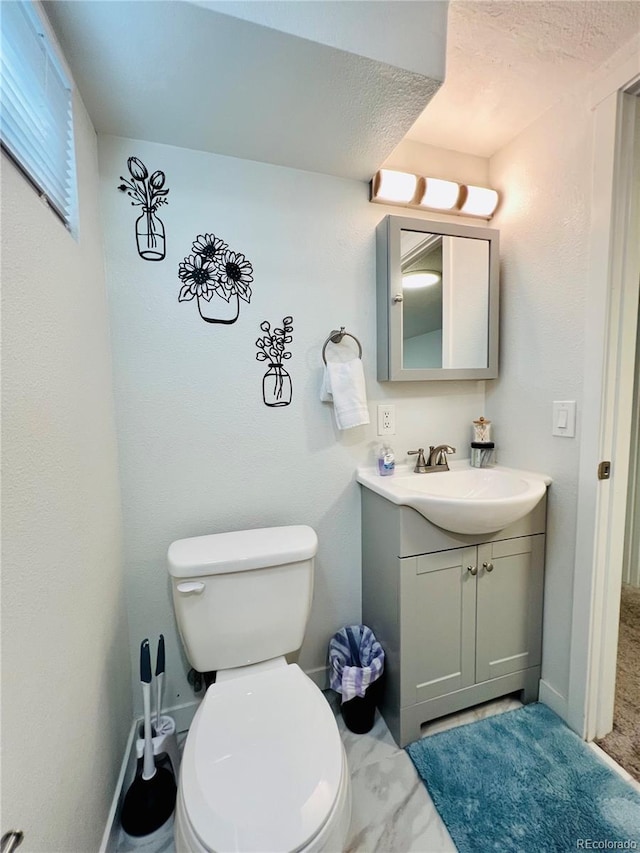 half bath featuring marble finish floor, baseboards, vanity, and toilet