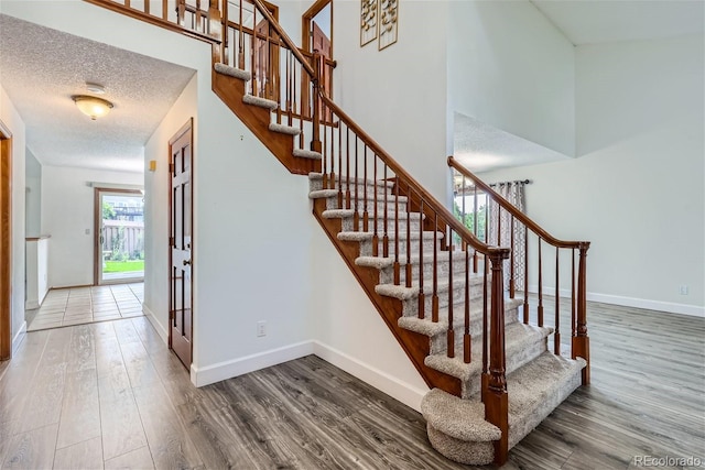 stairs featuring a high ceiling, a textured ceiling, baseboards, and wood finished floors