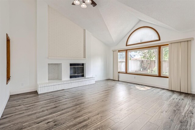 unfurnished living room with a textured ceiling, high vaulted ceiling, a fireplace, wood finished floors, and baseboards