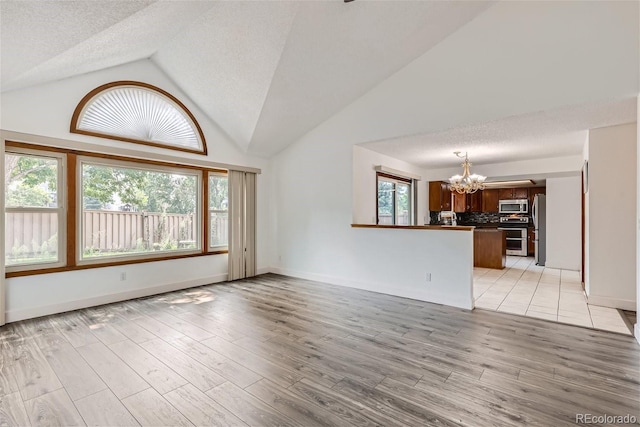 unfurnished living room with a wealth of natural light, vaulted ceiling, a notable chandelier, and light wood finished floors