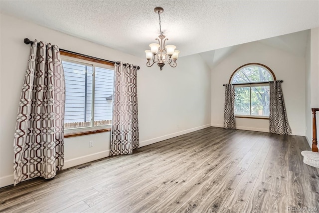 spare room with baseboards, wood finished floors, visible vents, and an inviting chandelier