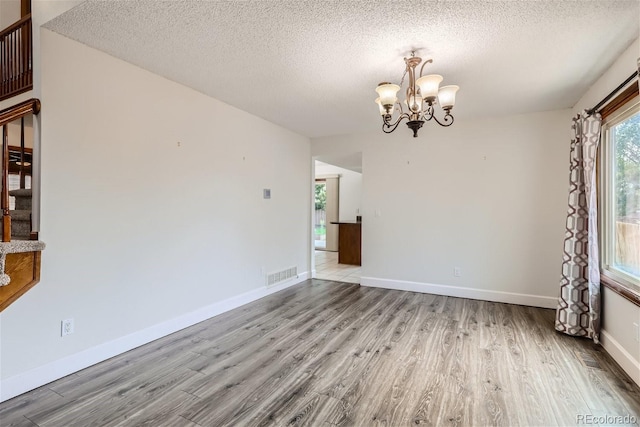 spare room with baseboards, visible vents, wood finished floors, stairs, and a chandelier