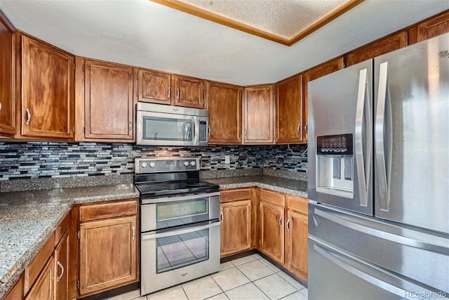 kitchen featuring brown cabinetry, dark countertops, appliances with stainless steel finishes, backsplash, and light tile patterned flooring