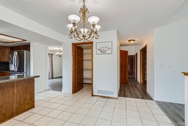 unfurnished dining area featuring an inviting chandelier, visible vents, a textured ceiling, and light tile patterned flooring