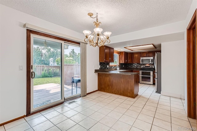 kitchen with light tile patterned flooring, stainless steel appliances, a peninsula, tasteful backsplash, and dark countertops