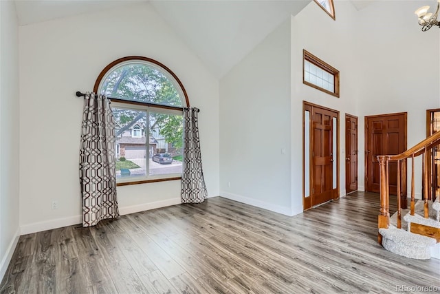 entryway featuring high vaulted ceiling, stairway, wood finished floors, a chandelier, and baseboards