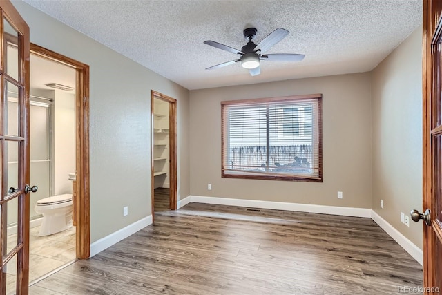 unfurnished bedroom featuring a spacious closet, baseboards, wood finished floors, and french doors