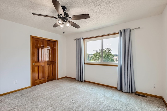 empty room with light colored carpet, visible vents, baseboards, and a textured ceiling