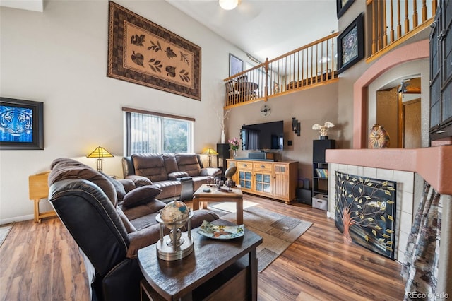 living room featuring a towering ceiling, a tile fireplace, wood finished floors, and baseboards