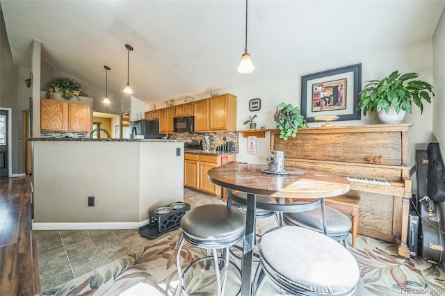 kitchen featuring black appliances, decorative backsplash, vaulted ceiling, decorative light fixtures, and brown cabinetry
