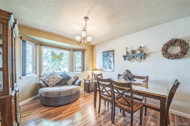 dining space featuring a chandelier, light wood-style flooring, baseboards, and a textured ceiling