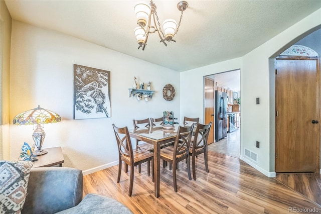 dining area featuring a chandelier, light wood finished floors, arched walkways, baseboards, and a textured ceiling