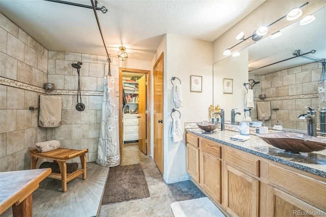 full bath featuring a tile shower, tile walls, a textured ceiling, double vanity, and a spacious closet