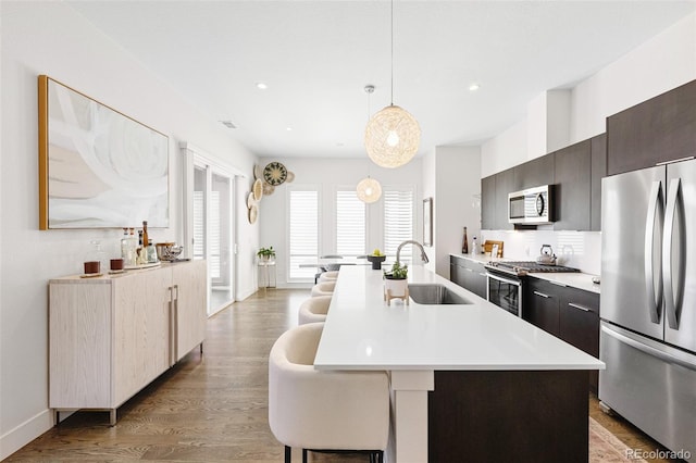 kitchen with wood finished floors, an island with sink, light countertops, a sink, and appliances with stainless steel finishes