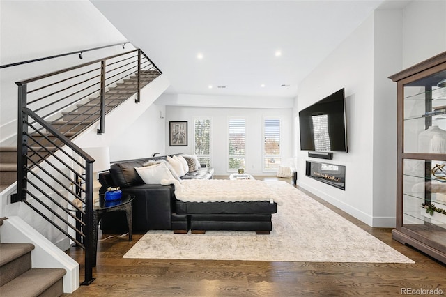 living area featuring a glass covered fireplace, baseboards, recessed lighting, and wood finished floors