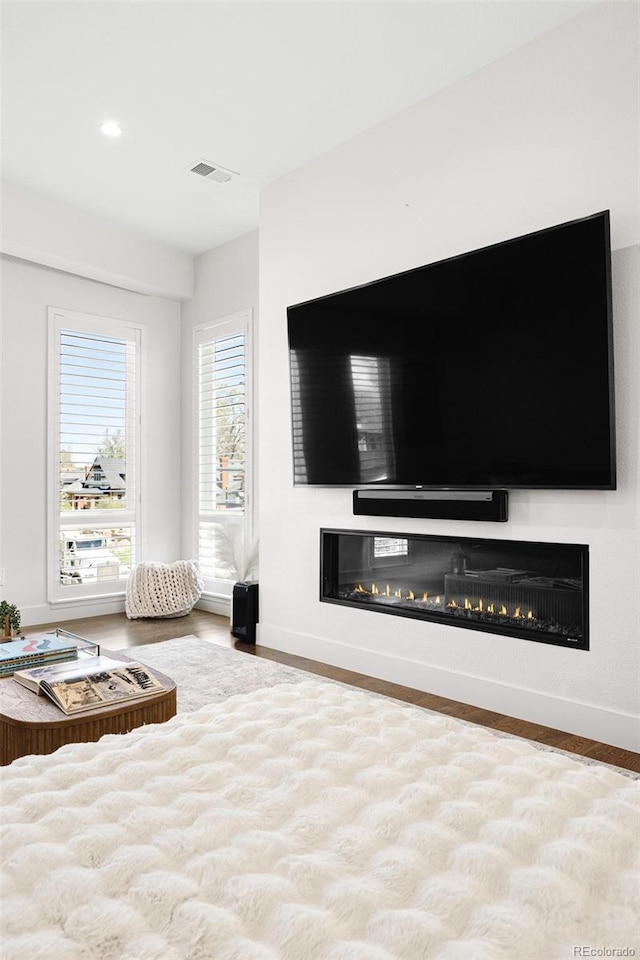 bedroom with visible vents, a glass covered fireplace, wood finished floors, baseboards, and recessed lighting