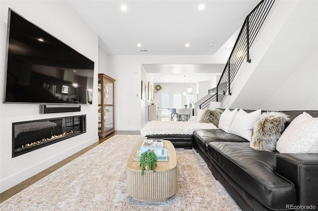 living room featuring a glass covered fireplace, stairs, recessed lighting, baseboards, and wood finished floors