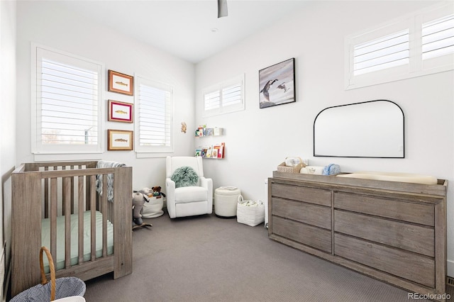 carpeted bedroom featuring a nursery area and ceiling fan