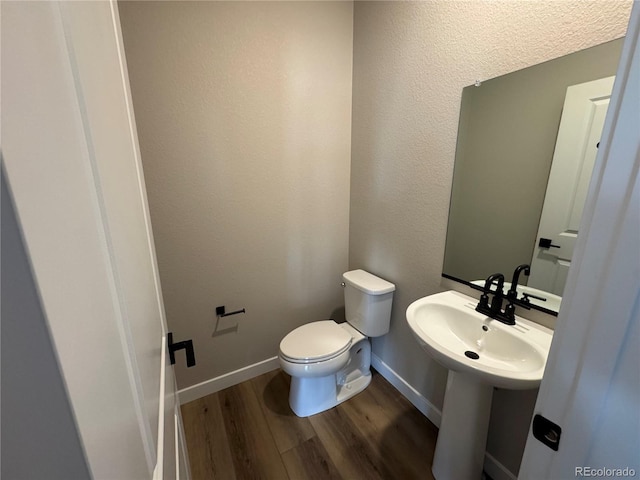 half bathroom featuring a sink, toilet, baseboards, and wood finished floors