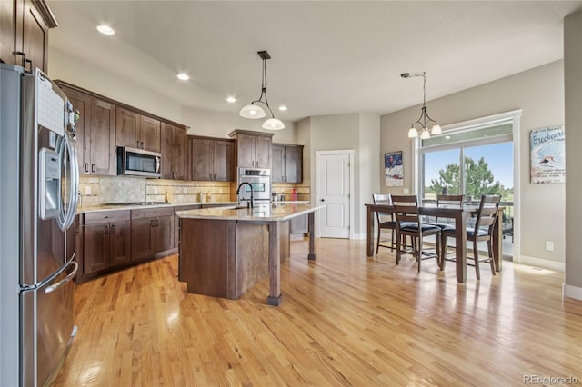 7258 Spanish Bay Dr, Windsor, CO 80550 - kitchen featuring stainless steel appliances, tasteful backsplash, a breakfast bar, light wood finished floors, and dark brown cabinets