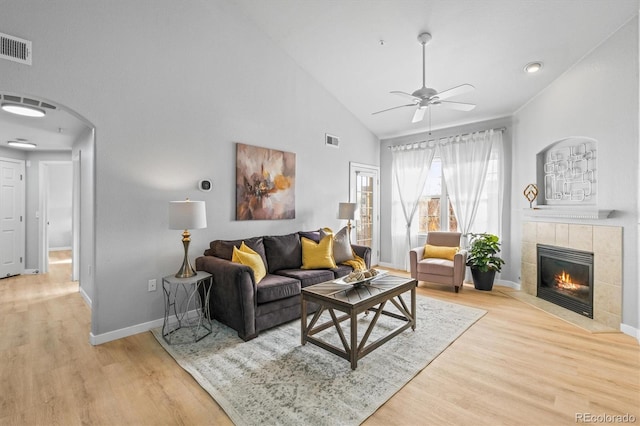 living room featuring high vaulted ceiling, ceiling fan, light wood-type flooring, and a tile fireplace