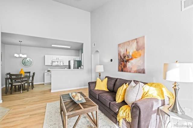 living room featuring a towering ceiling, a notable chandelier, and light wood-type flooring