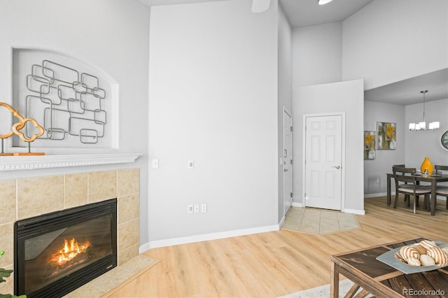 living room featuring an inviting chandelier, wood-type flooring, high vaulted ceiling, and a tiled fireplace