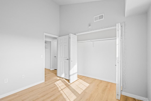 unfurnished bedroom featuring a closet, a towering ceiling, and light hardwood / wood-style floors