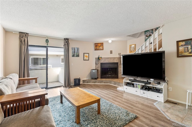 living room with a tiled fireplace, light hardwood / wood-style floors, and a textured ceiling