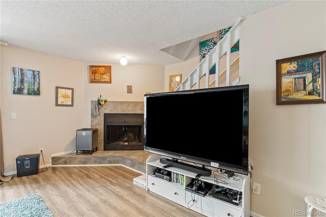 living room featuring a tiled fireplace, a textured ceiling, and light wood-type flooring