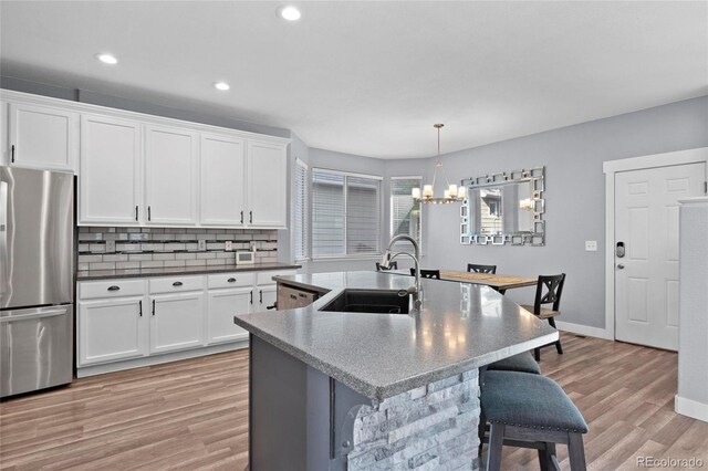 kitchen featuring freestanding refrigerator, a sink, a kitchen bar, a chandelier, and light wood-style floors