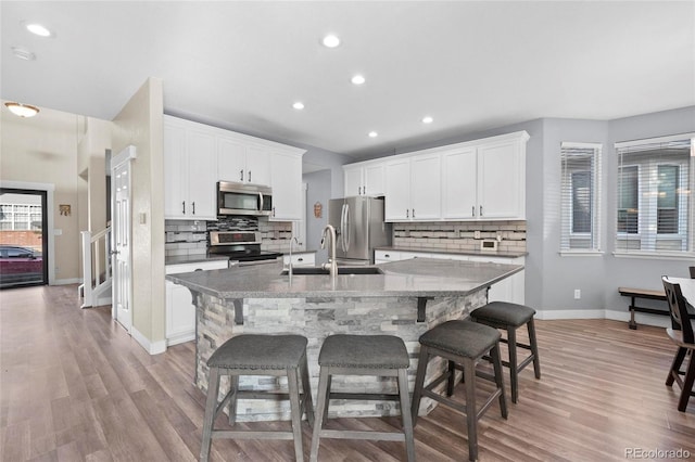 kitchen featuring appliances with stainless steel finishes, an island with sink, decorative backsplash, a breakfast bar, and baseboards