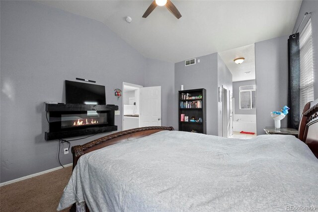 carpeted bedroom with vaulted ceiling, a glass covered fireplace, ensuite bathroom, baseboards, and a ceiling fan