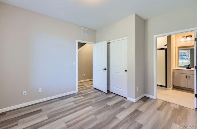 unfurnished bedroom featuring connected bathroom, a closet, and light wood-type flooring