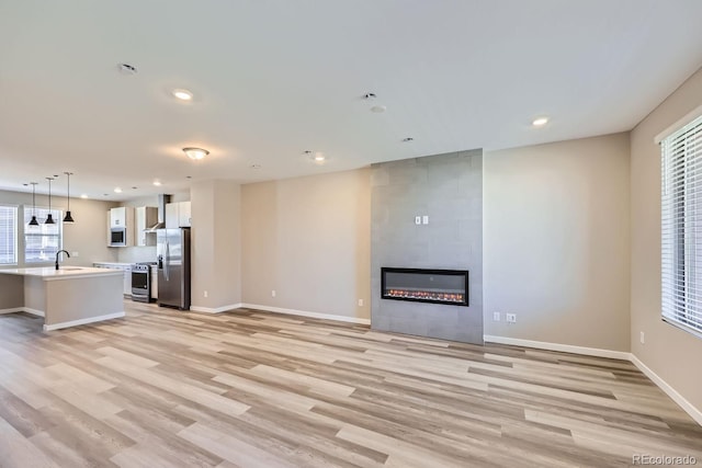 unfurnished living room with sink, a tile fireplace, and light hardwood / wood-style flooring