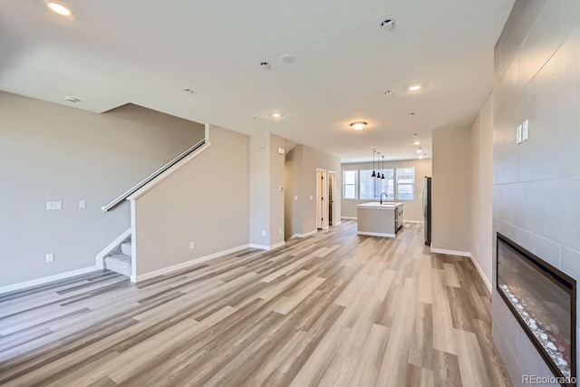 unfurnished living room with a tile fireplace, light wood-type flooring, and sink