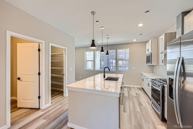 kitchen with appliances with stainless steel finishes, light wood-type flooring, sink, decorative light fixtures, and an island with sink