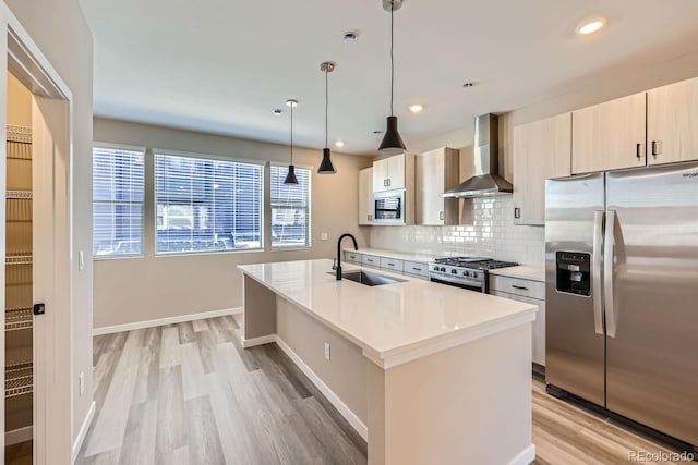 kitchen with sink, wall chimney exhaust hood, an island with sink, pendant lighting, and appliances with stainless steel finishes