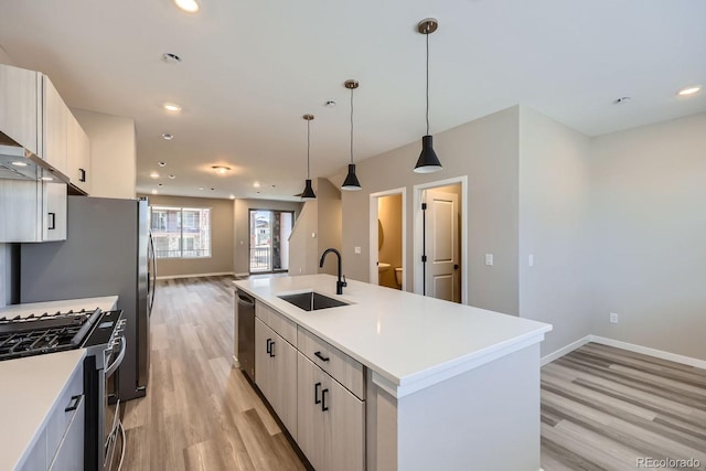 kitchen with sink, decorative light fixtures, a center island with sink, appliances with stainless steel finishes, and light wood-type flooring