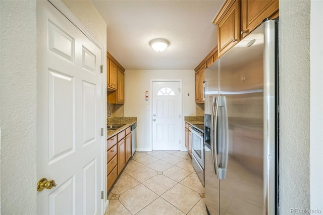 kitchen featuring stainless steel appliances, brown cabinets, stone countertops, light tile patterned flooring, and a textured wall
