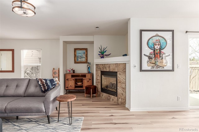 living area with light wood-style floors, visible vents, a tiled fireplace, and baseboards