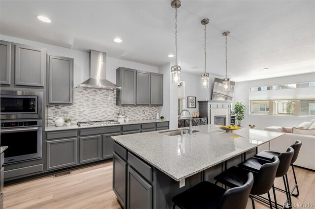 13736 Umatilla Ln, Broomfield, CO 80023 - kitchen featuring appliances with stainless steel finishes, wall chimney range hood, gray cabinets, open floor plan, and decorative backsplash