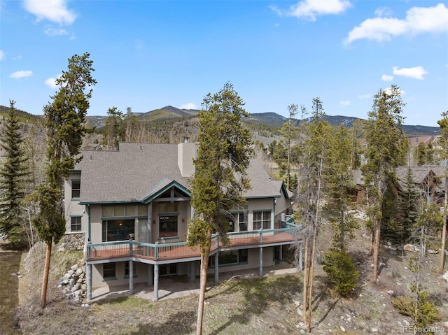 rear view of house featuring a mountain view, a shingled roof, a chimney, and stucco siding