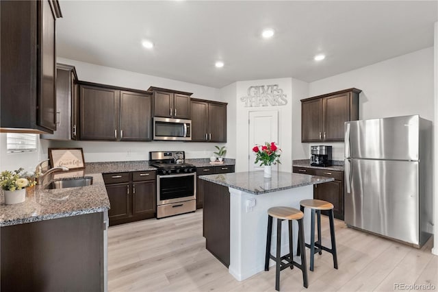 kitchen with a center island, dark stone counters, sink, light wood-type flooring, and stainless steel appliances