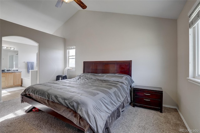 bedroom with ceiling fan, vaulted ceiling, light colored carpet, and ensuite bath